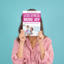 Load image into Gallery viewer, woman in pink shirt with blue background holding book less stress more joy for moms
